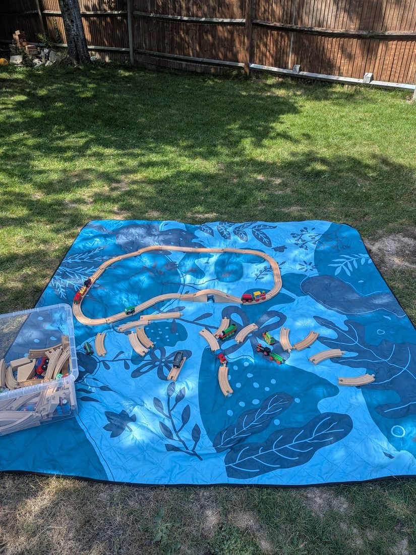 Wooden train track set out on a play mat in the garden